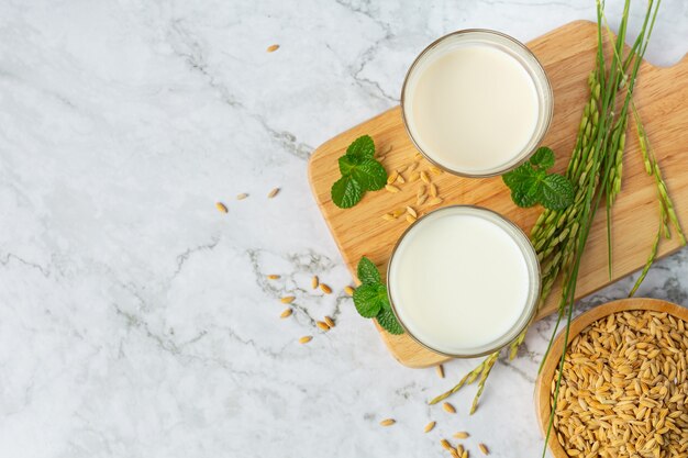 Dois copos de leite de arroz com planta de arroz na borda de madeira ao lado da tigela de sementes de arroz