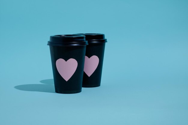 Dois copos de papel preto para bebidas quentes com corações rosa no azul