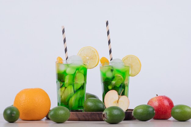 Dois copos de suco com fatias de frutas e frutas frescas.