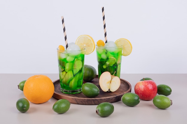 Dois copos de suco com fatias de frutas e frutas frescas.