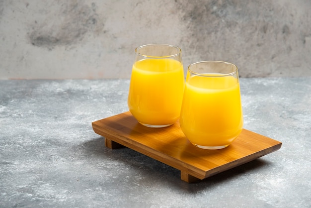 Dois copos de suco de laranja fresco na placa de madeira.