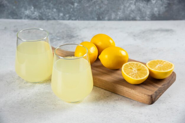 Dois copos de vidro de limonada saborosa em uma placa de madeira.