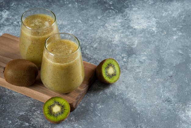 Dois copos de vidro de saboroso suco de kiwi na placa de madeira.