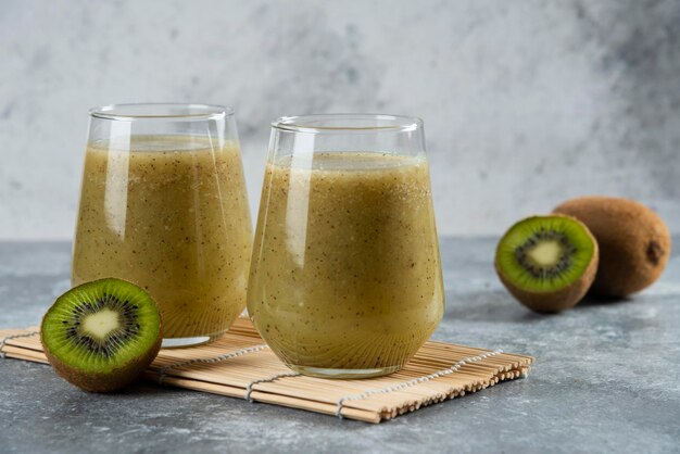 Dois copos de vidro de suco de kiwi fresco na folha de bambu.