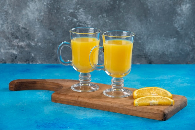 Dois copos de vidro de suco de laranja na placa de madeira.