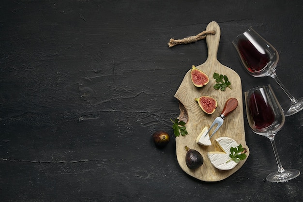 Dois copos de vinho tinto e um saboroso prato de queijo com frutas em um prato de madeira de cozinha na pedra preta