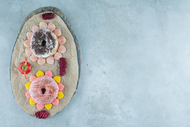 Foto grátis dois donuts rodeados de marmeladas em uma placa de madeira no mármore.