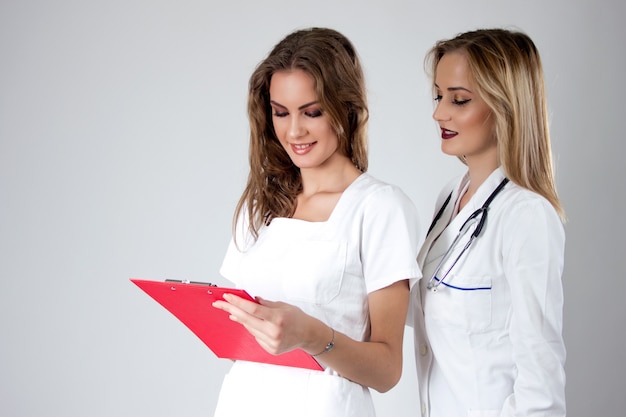 Foto grátis dois doutores das mulheres consideravelmente novas, enfermeiras que olham através do registro médico do paciente.