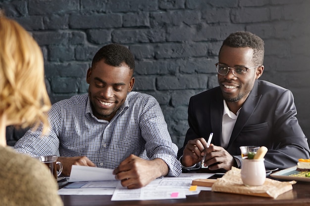 Dois empregadores de pele escura entrevistando uma jovem de cabelos louros durante uma entrevista de emprego