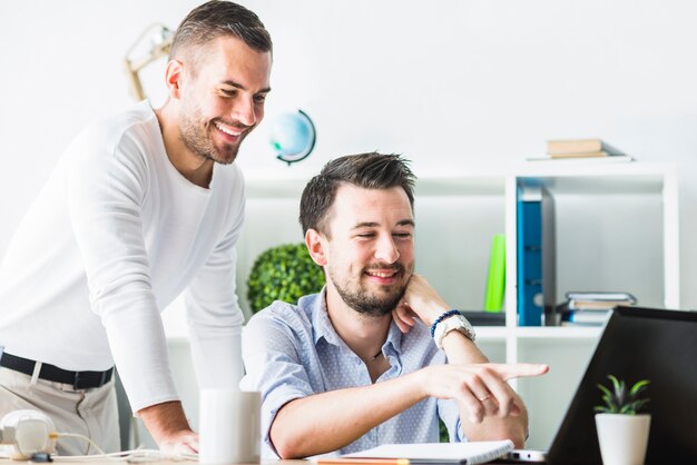 Dois empresários jovens sorridentes, olhando para a tela do laptop