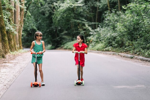 Dois, femininas, amigos, com, scooters, olhando um ao outro, ligado, estrada