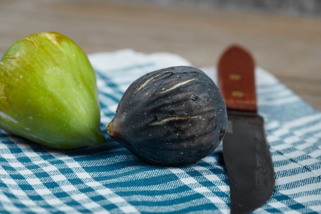 Dois figos e uma faca com uma toalha de mesa azul na mesa de madeira.