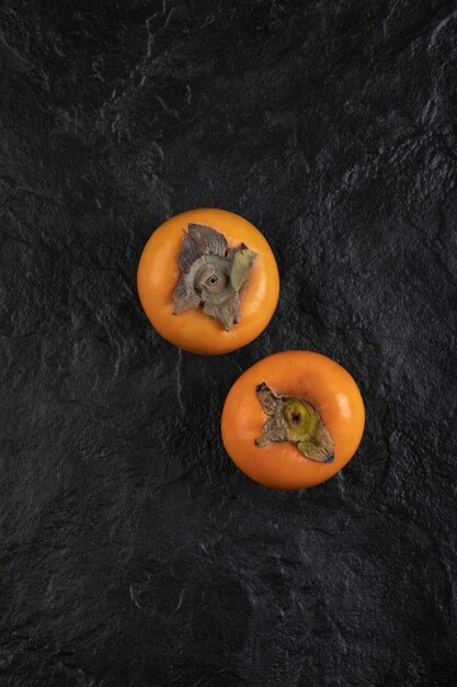 Dois frutos maduros de caqui colocados na superfície preta