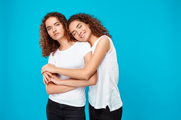 Foto grátis dois gêmeos da jovem mulher abraçando, sorrindo sobre o azul.