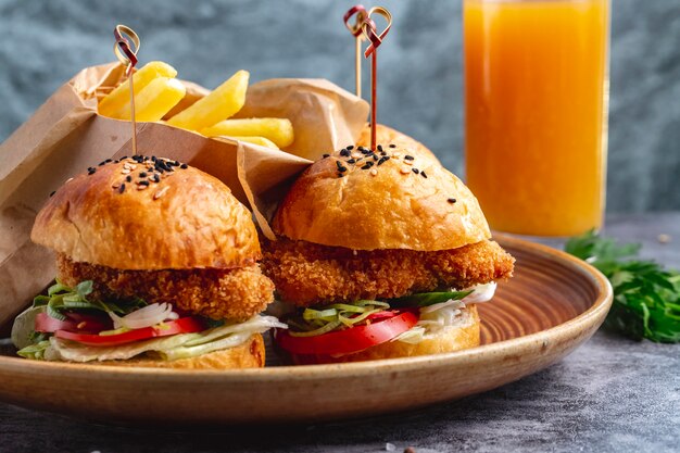 Dois hambúrgueres de mini nuggets de frango servidos com batatas fritas em caixa de papel