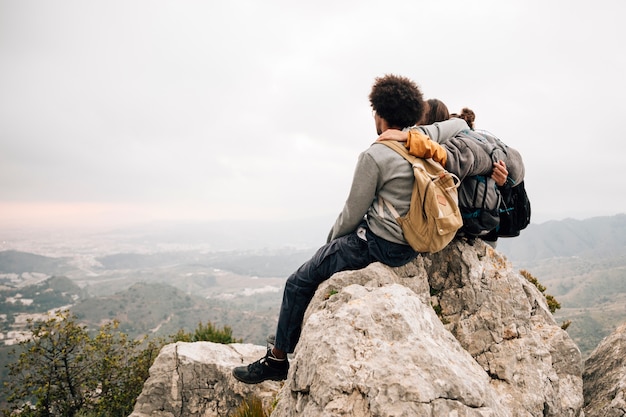 Dois, hiker masculino, sentar, cima, rocha, sobre, a, montanha, olhar, vista cênica