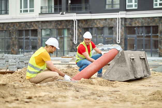 Dois homens agachados perto do tubo no canteiro de obras