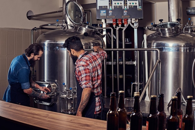 Dois homens hipster barbudo em um avental trabalhando na fábrica de cervejaria.