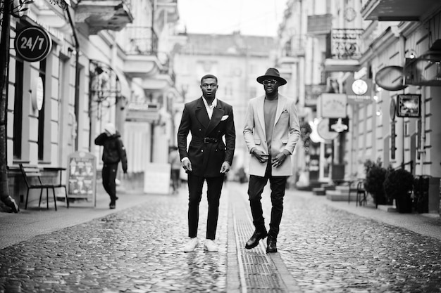 Dois homens negros da moda andando na rua retrato da moda de modelos masculinos afro-americanos usar casaco e chapéu