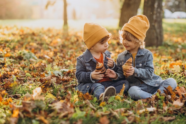 Dois irmãos meninos sentados na grama do parque comendo croissants