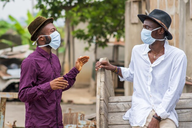 Dois jovens amigos afro-americanos com máscaras protetoras rindo e se distanciando socialmente