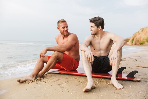 Dois jovens bonitos e sorridentes relaxando em uma praia com uma prancha de surf