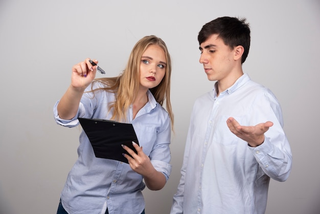 Dois jovens colegas de escritório discutindo um projeto na parede cinza.