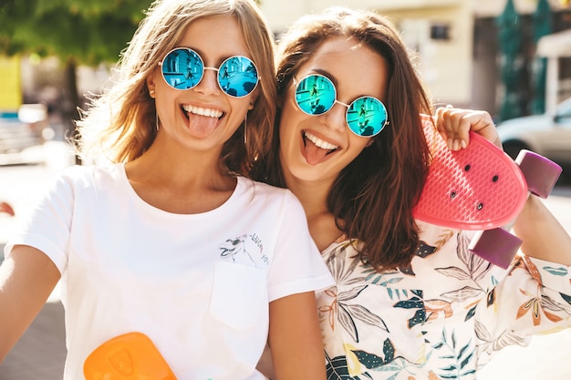 Dois jovens elegantes sorrindo morena hippie em dia ensolarado de verão em roupas hipster com posando de skate centavo