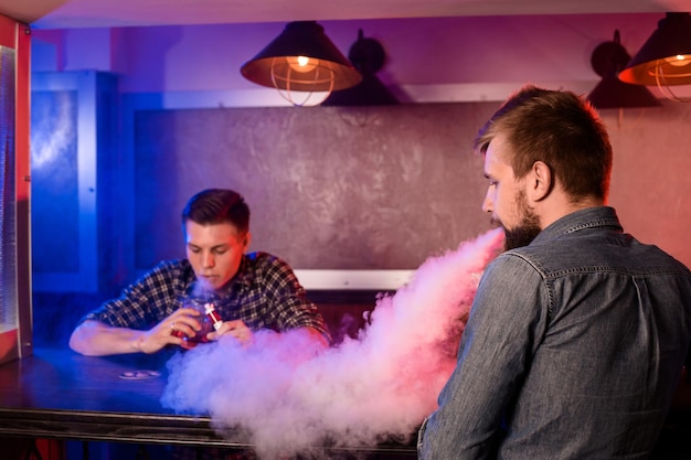 Foto grátis dois jovens fumam cigarros eletrônicos em um vapebar. loja de vaporizadores