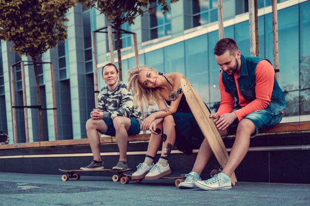 Dois machos e uma fêmea com longboards posando na rua em estilo urbano.