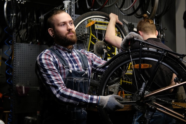 Dois machos elegantes bonitos trabalhando com uma bicicleta em uma oficina. Os trabalhadores reparam e montam a bicicleta em uma oficina.