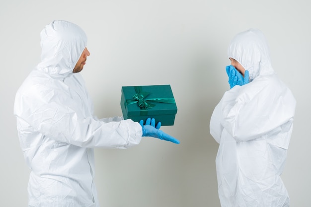 Dois médicos dando uma caixa de presente um ao outro em traje de proteção