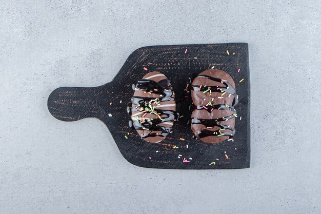 Dois mini bolos de chocolate com granulado na tábua de corte preta. Foto de alta qualidade