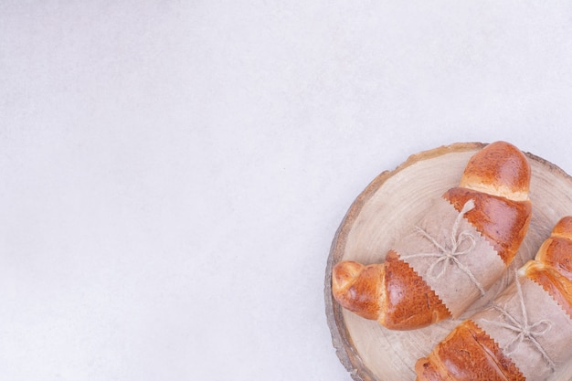 Dois pães de croissant em embrulho de papel na placa de madeira.