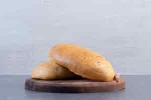 Foto grátis dois pães e um único talo de trigo em uma placa de madeira com fundo de mármore. foto de alta qualidade