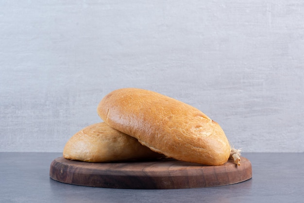 Dois pães e um único talo de trigo em uma placa de madeira com fundo de mármore. Foto de alta qualidade