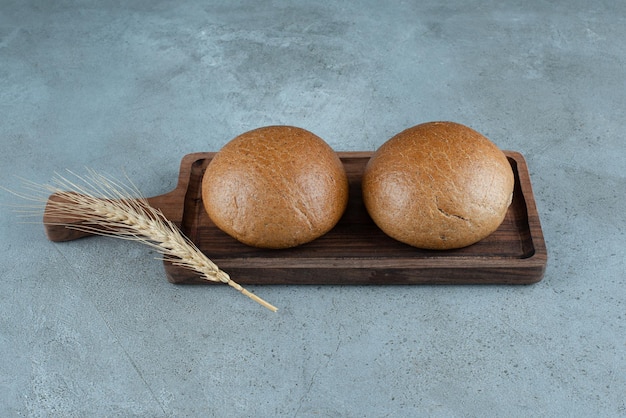 Dois pães frescos na placa de madeira com trigo.
