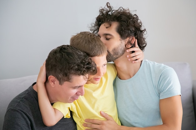 Dois pais bonitos felizes abraçando e beijando o filho, aproveitando o tempo de lazer juntos. família feliz e conceito de pais gays