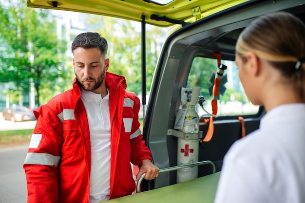 Dois paramédicos com uma maca perto de uma ambulância paramédicos de uniforme tirando maca do carro da ambulância