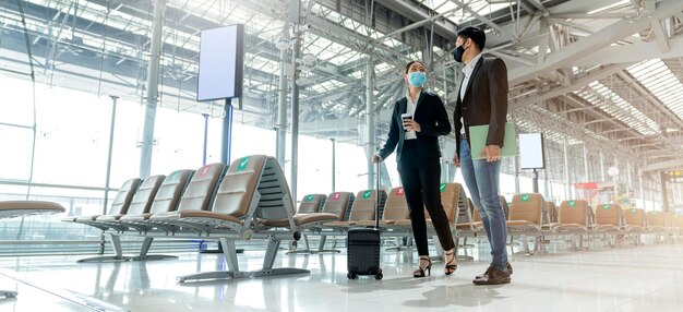 Dois parceiros de negócios asiáticos com proteção de máscara facial distanciamento social novo estilo de vida normal Viajantes de negócios andando no aeroporto com bagagem