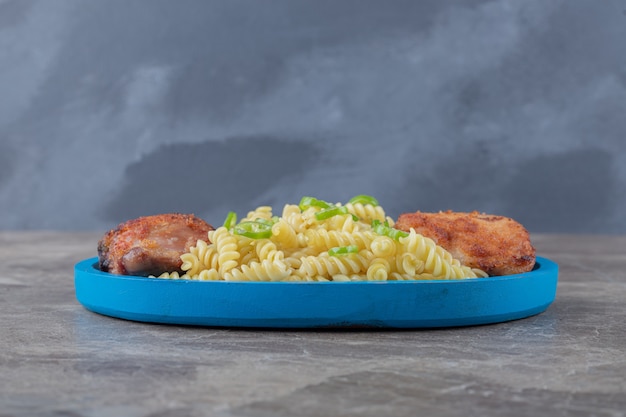 Foto grátis dois pedaços de carne e macarrão fusilli apimentado na bandeja de madeira, sobre a superfície de mármore.