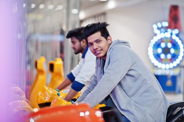 Foto grátis dois rapazes asiáticos competem na máquina de simulador de corridas de moto de jogo de arcade de velocidade