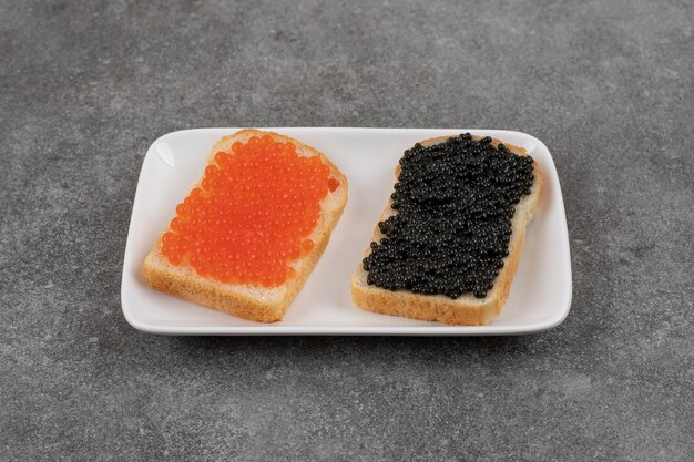 Dois sanduíches com caviar vermelho e preto no branco preto.