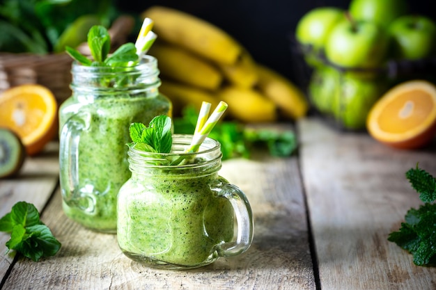 Dois smoothies verdes saudáveis com espinafre, banana, maçã, kiwi e hortelã em frasco de vidro e ingredientes dieta de desintoxicação conceito de comida vegetariana saudável