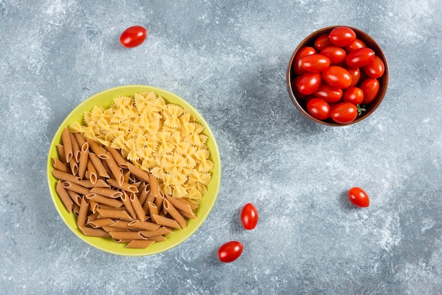 Dois tipos de massa crua no prato com tigela de tomates.