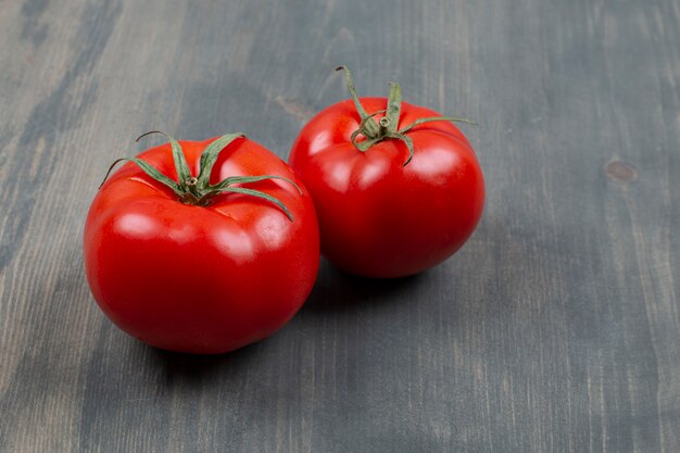 Dois tomates frescos crus com folhas em uma mesa de madeira