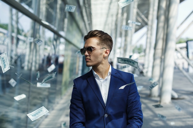 Dólares voam em torno de bonito jovem empresário enquanto ele caminha ao longo da rua