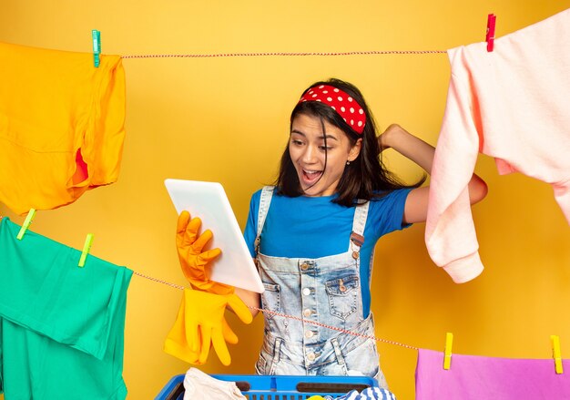 Dona de casa linda e engraçada fazendo trabalhos domésticos isolados no espaço amarelo. Jovem mulher caucasiana rodeada de roupas lavadas