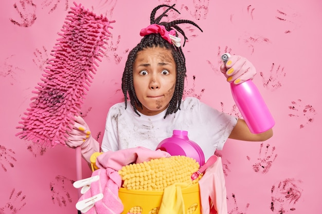 Foto grátis dona de casa nervosa e desarrumada aperta os lábios deixa a casa em ordem limpa o quarto segura o esfregão e o detergente de limpeza não quer que o apartamento sujo recolhe roupa suja isolada sobre a parede rosa