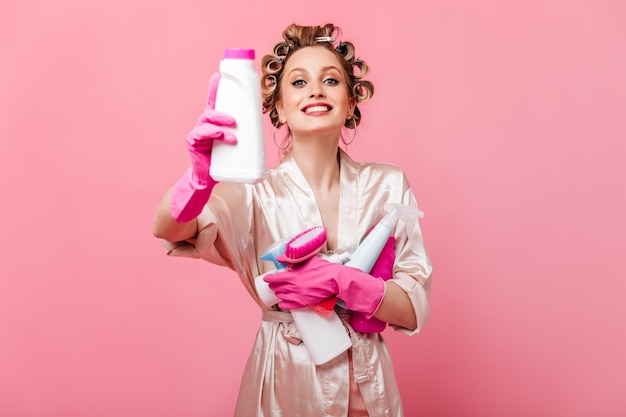 Dona de casa positiva em roupa de seda segurando escovas e detergentes